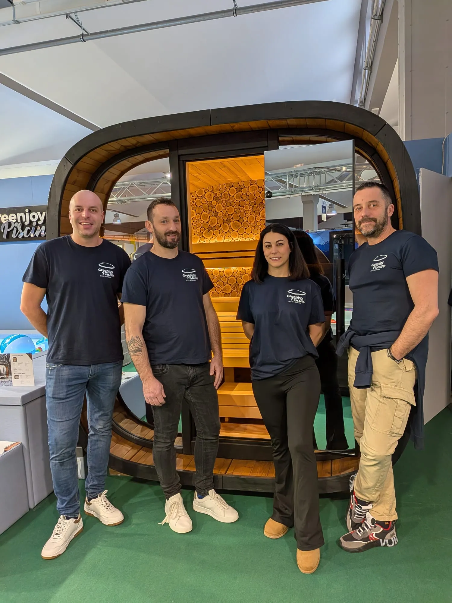 Il team Greenjoy al proprio stand fieristico, davanti a una sauna e alle spa esposte