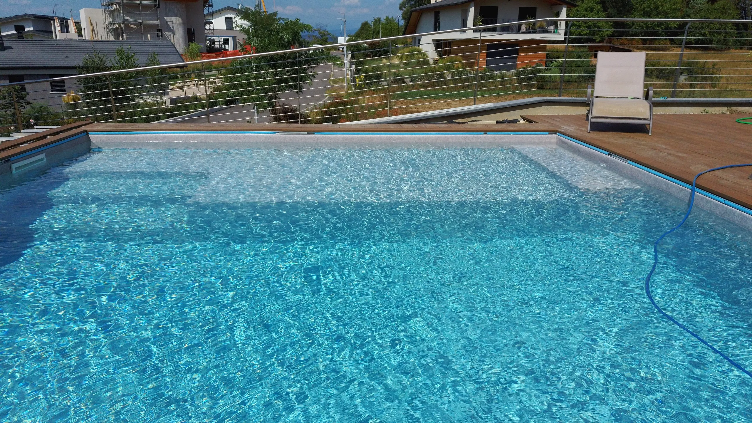 Piscina con l’acqua cristallina e il tubo della pulizia del fondo appoggiato sul bordo