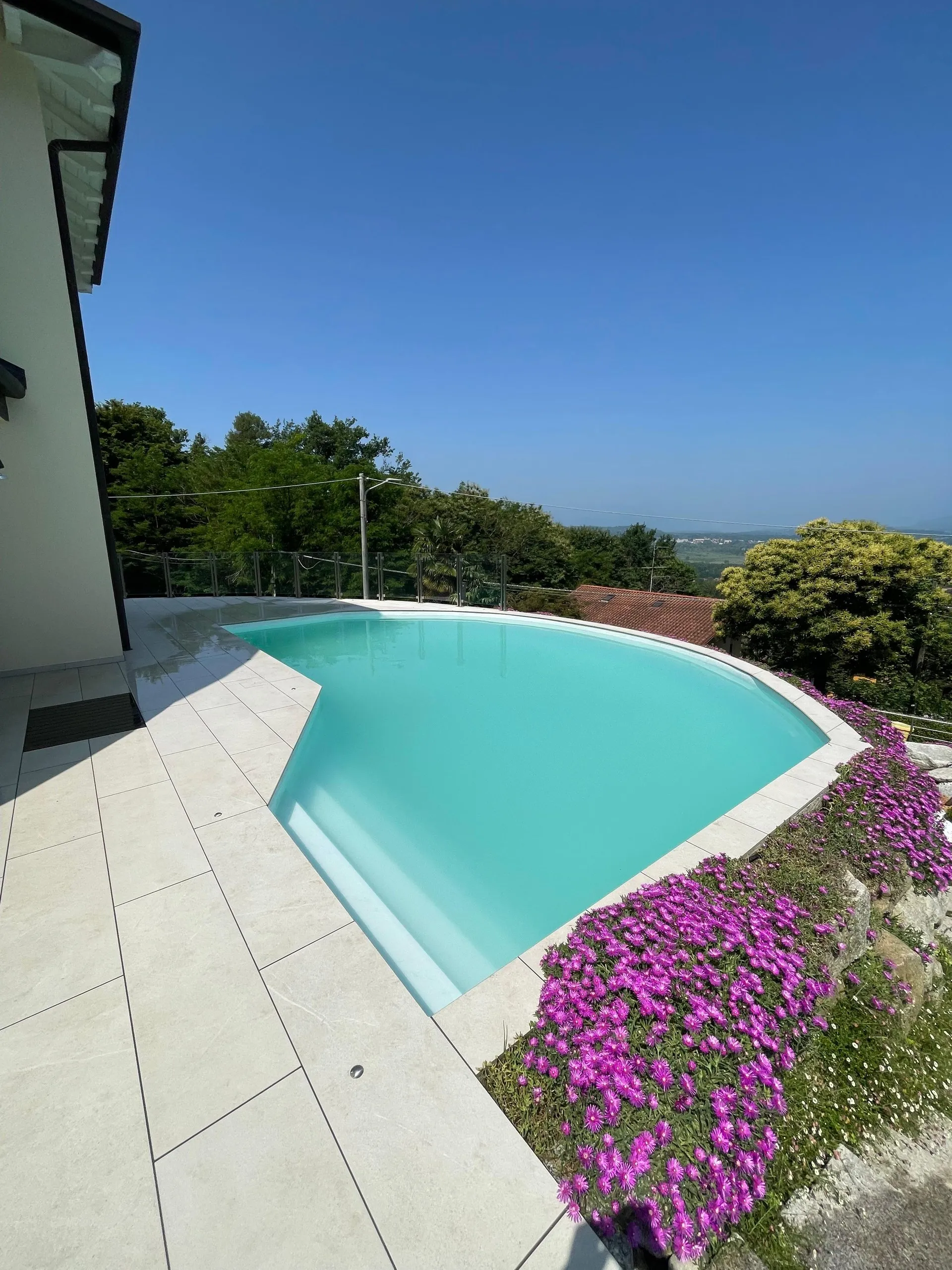 Piscina con l’acqua limpida e la scala romana, affiancata da un’aiuola di fiori viola in primavera