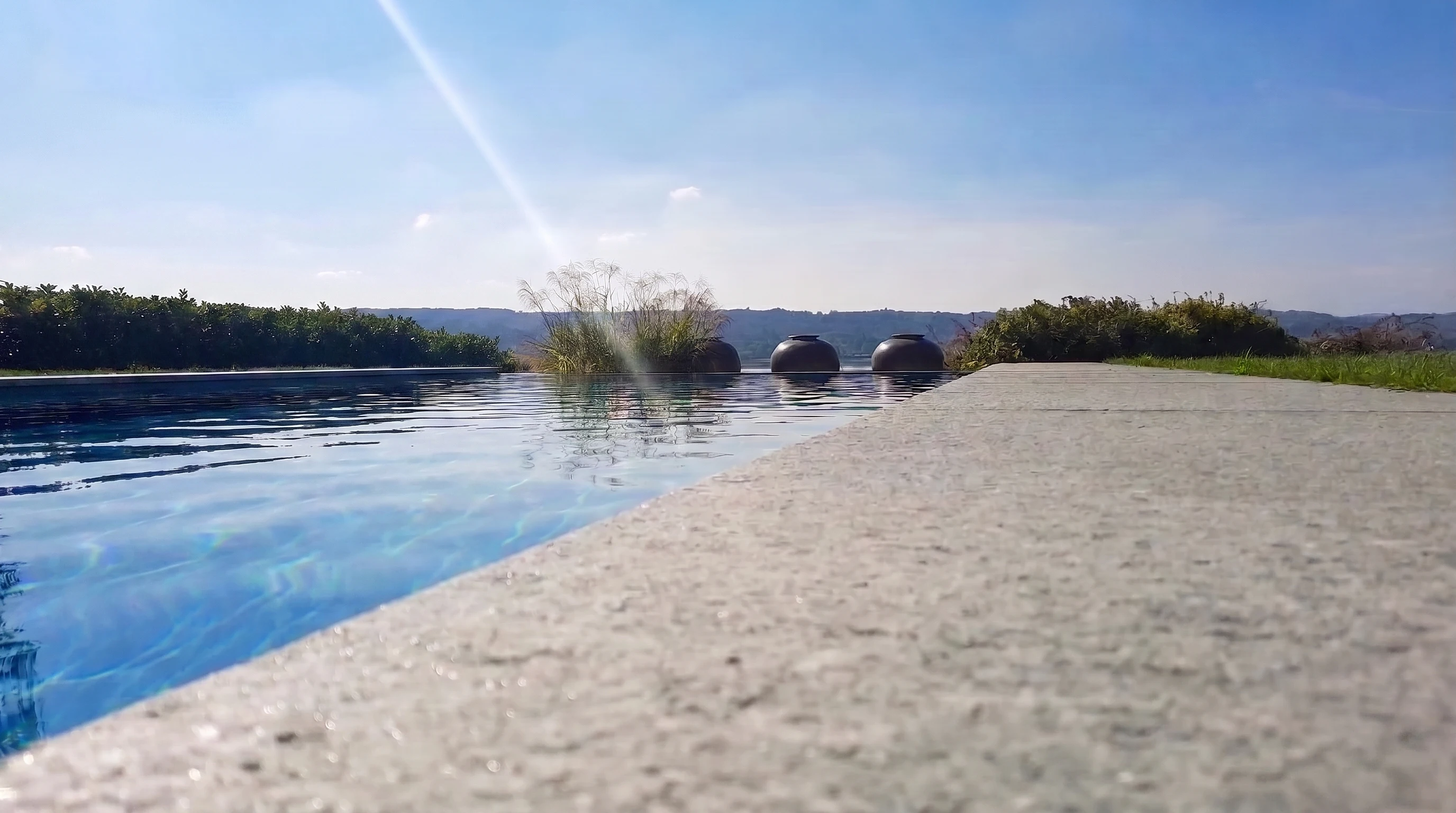 Piscina a sfioro vista da vicino, con acqua blu e bordo chiaro verso le colline